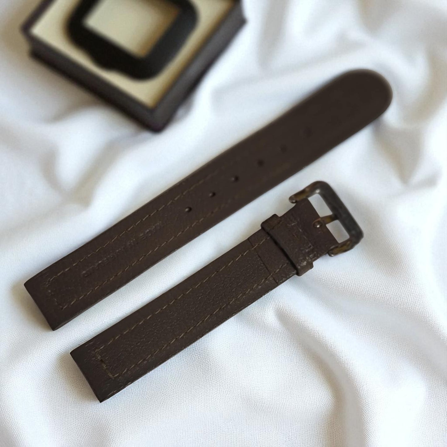 Brown watch strap on a white fabric background