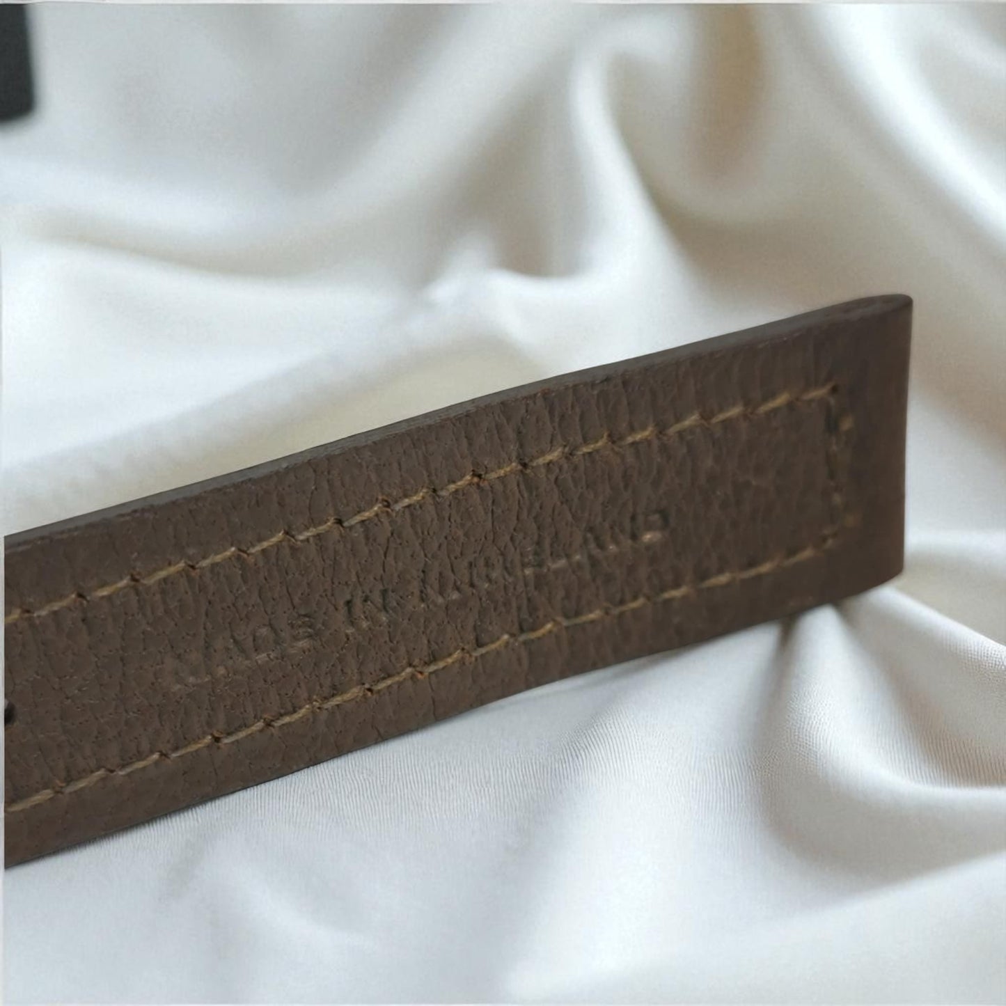 Brown leather belt with visible stitching on a white fabric background