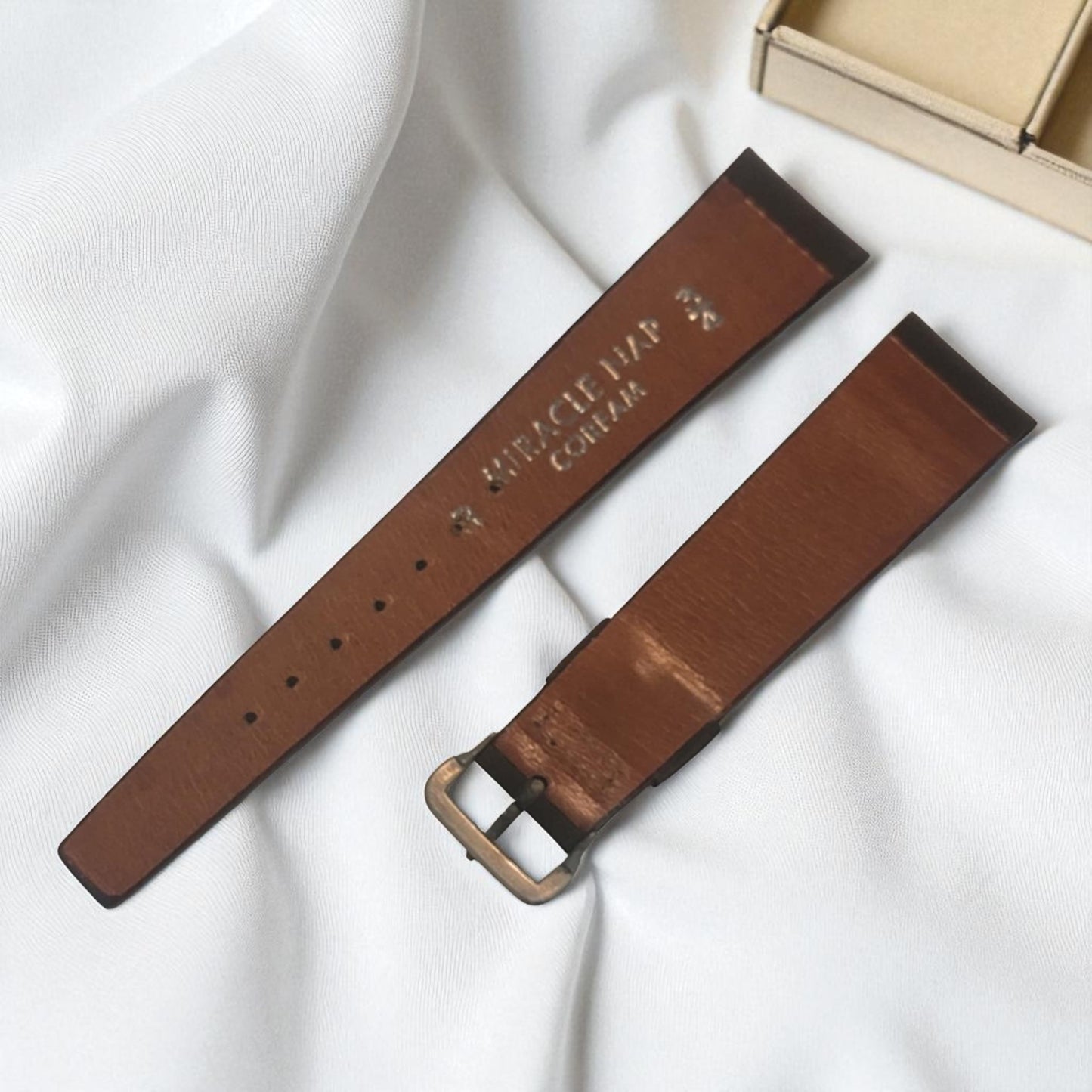 Brown leather strap with gold buckle on a white fabric background