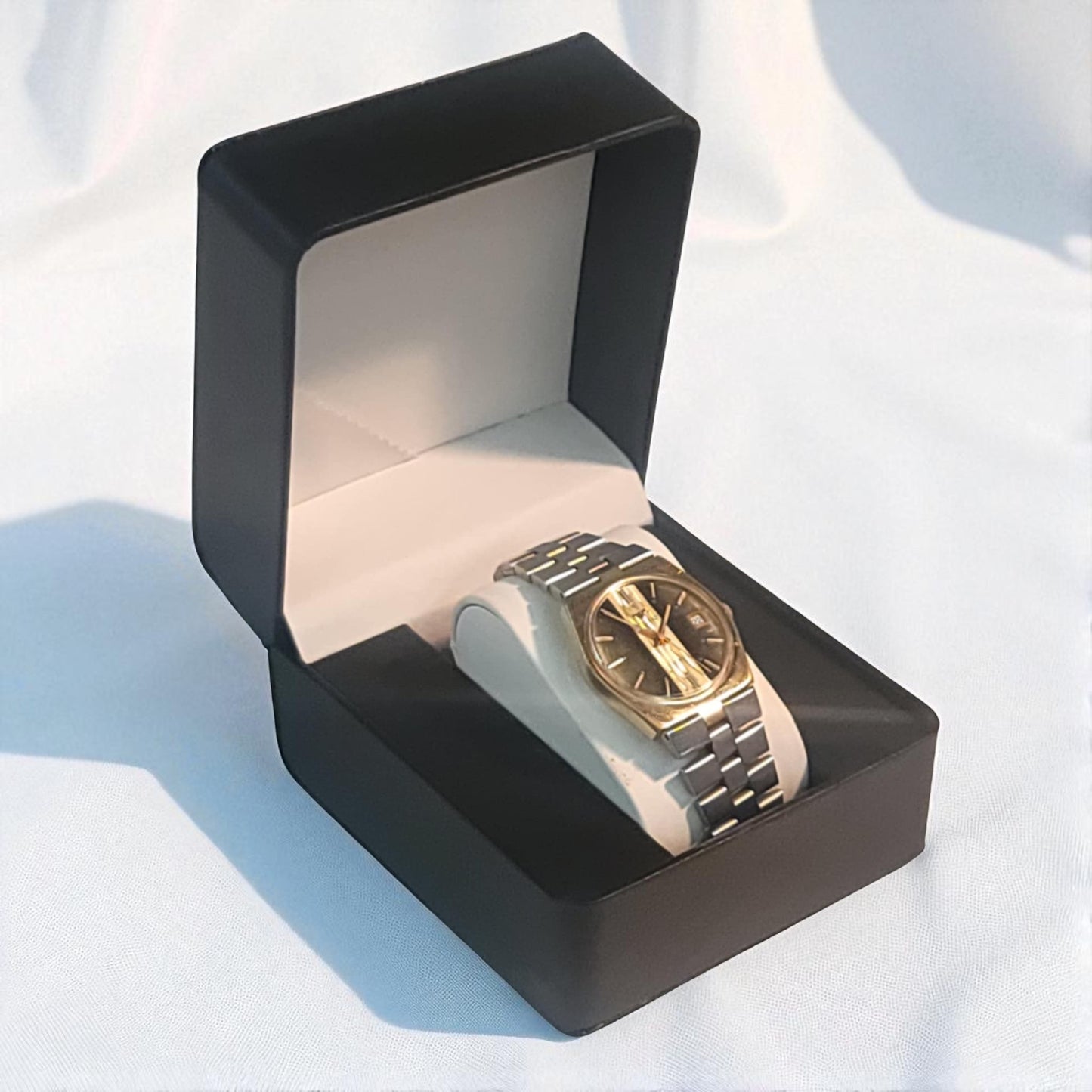 Gold watch in a black display box on a light blue background