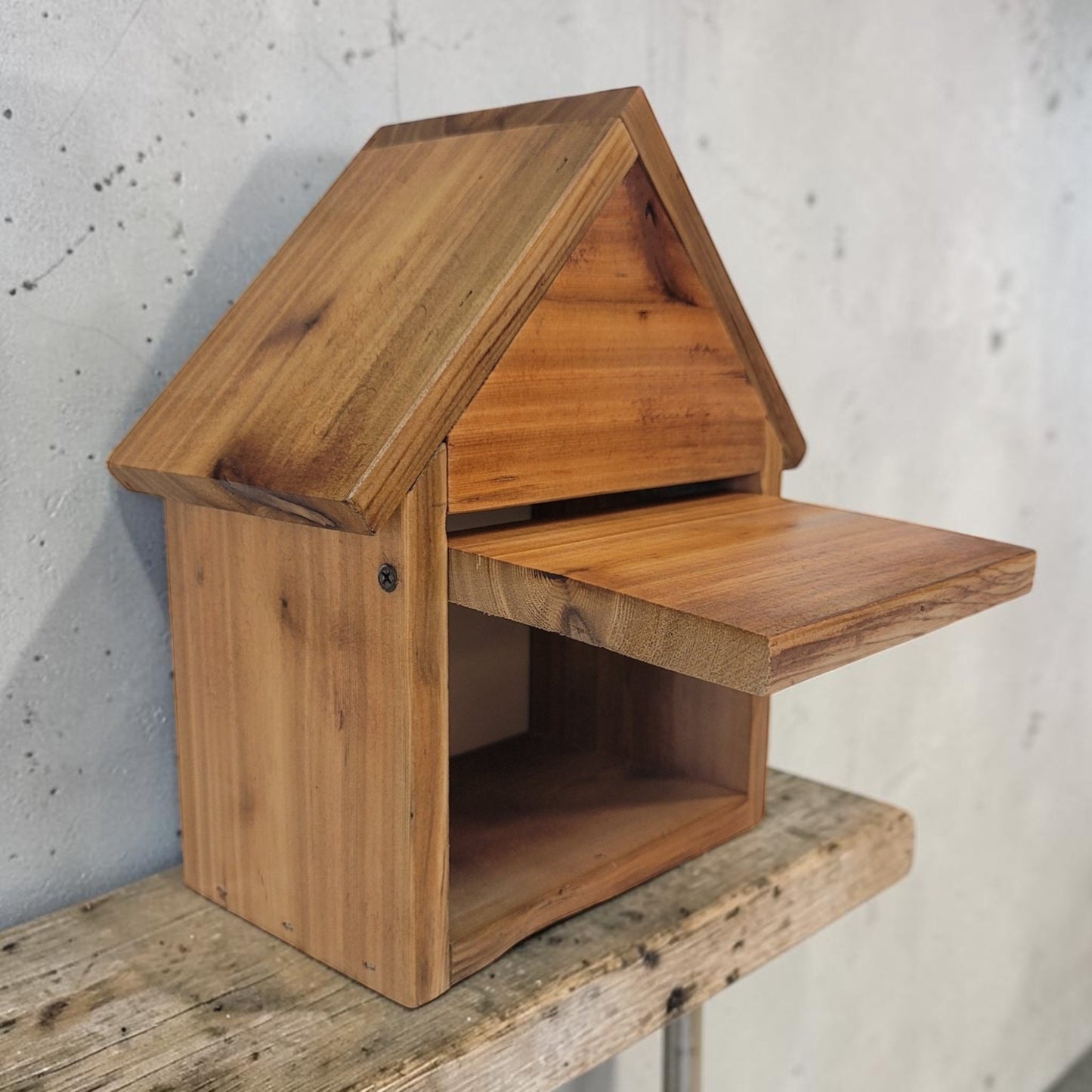 Wooden birdhouse on a wooden surface with a concrete wall background