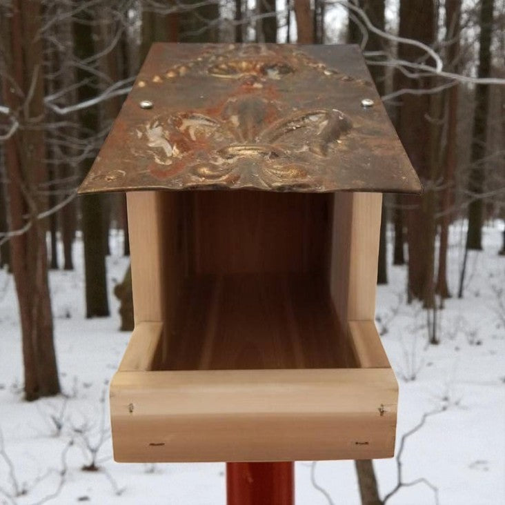 Wooden bird feeder with a decorative metal top in a snowy forest setting