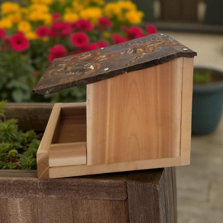 Wooden bird feeder on a post with flowers in the background