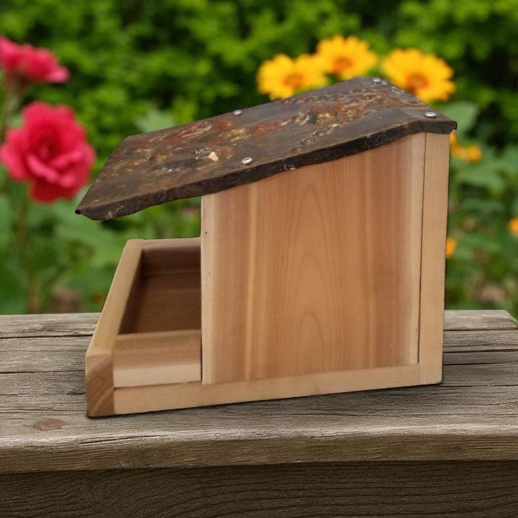 Wooden bird feeder on a wooden surface with flowers in the background
