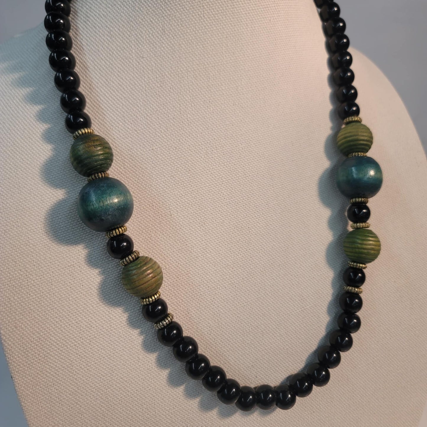 Necklace with black, green, and gold beads on a mannequin.