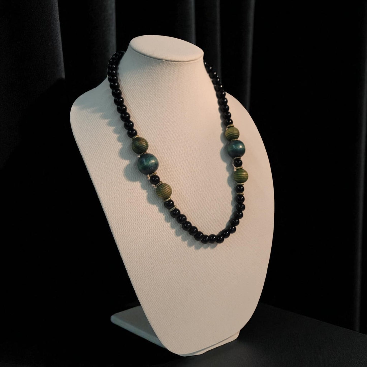Necklace with black and green beads on a white bust against a black background