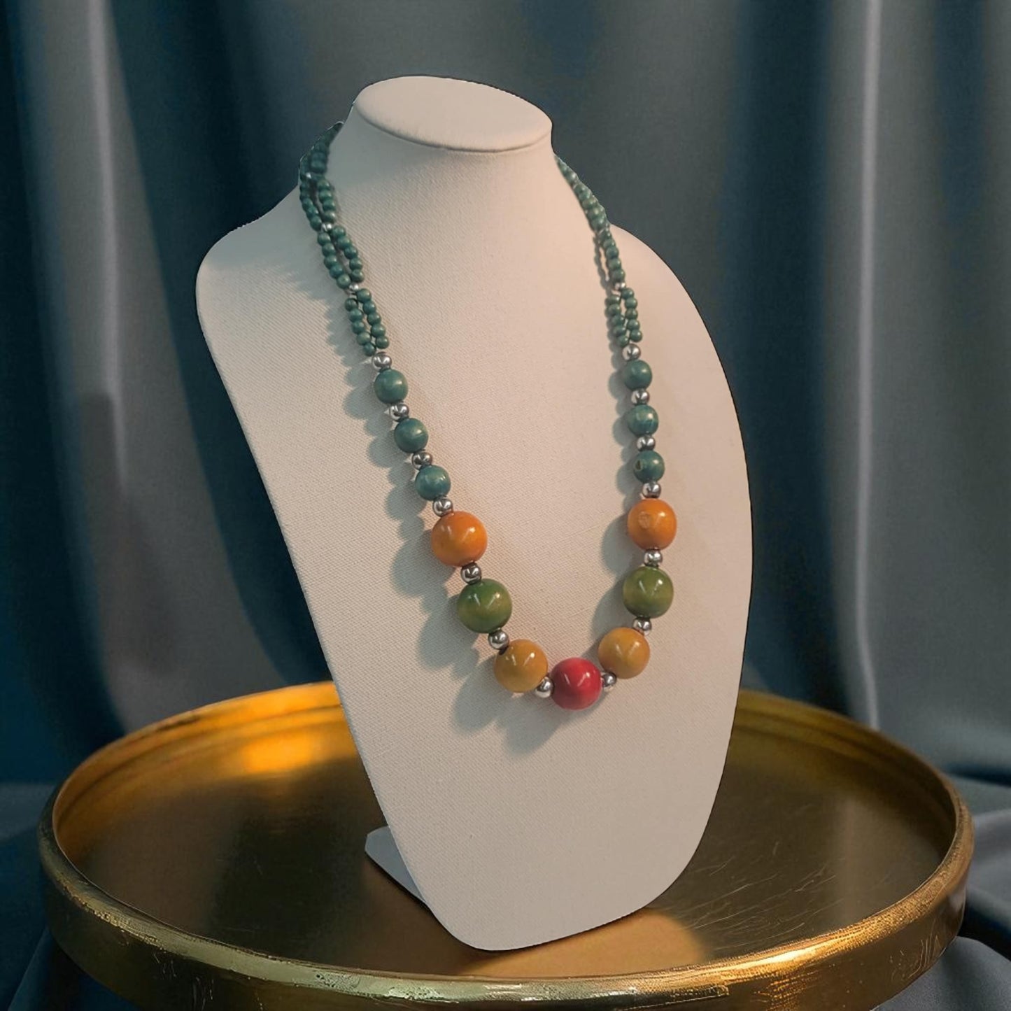 Necklace with multicolored beads on a white bust against a dark curtain background