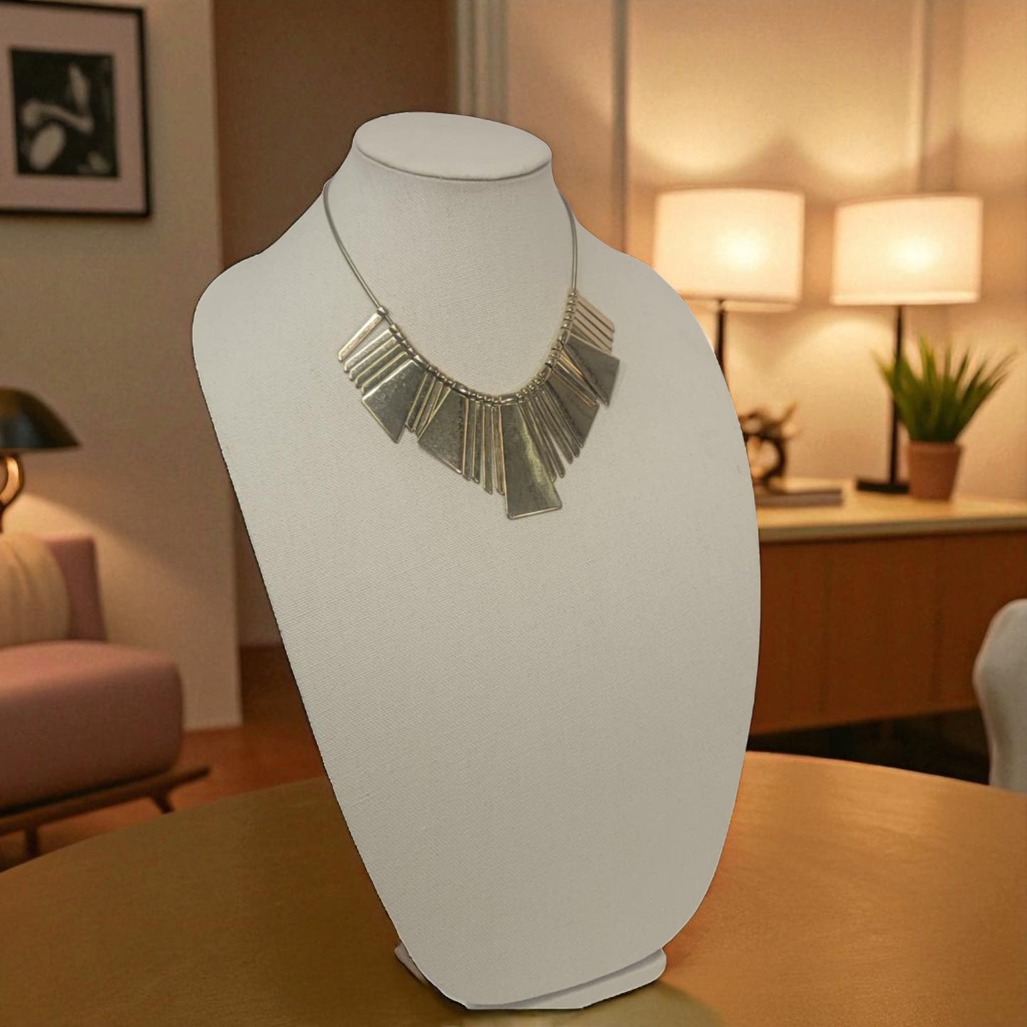 Silver necklace on a mannequin bust in a room with lamps and a plant.