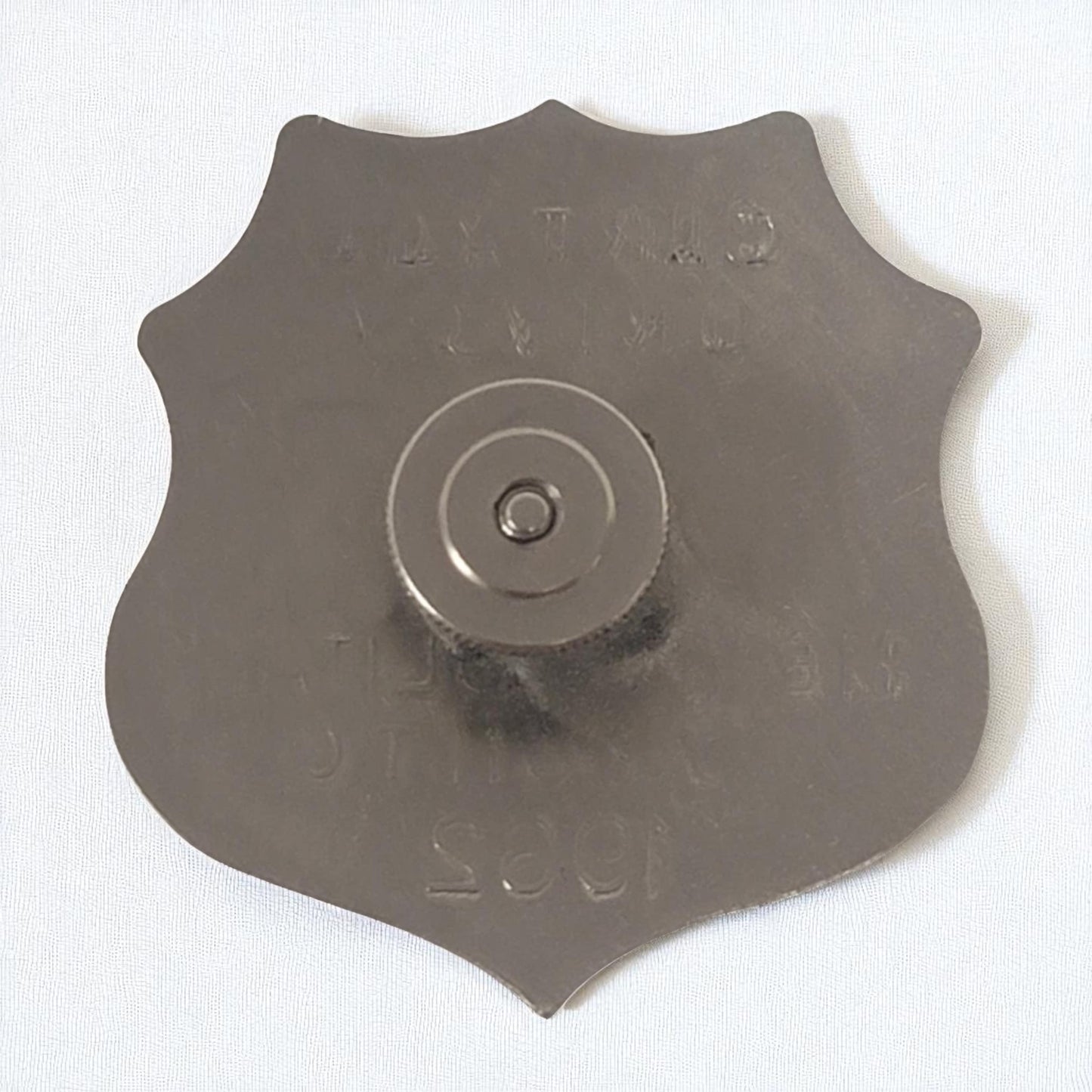 Metal shield-shaped object with central circular component on a white background