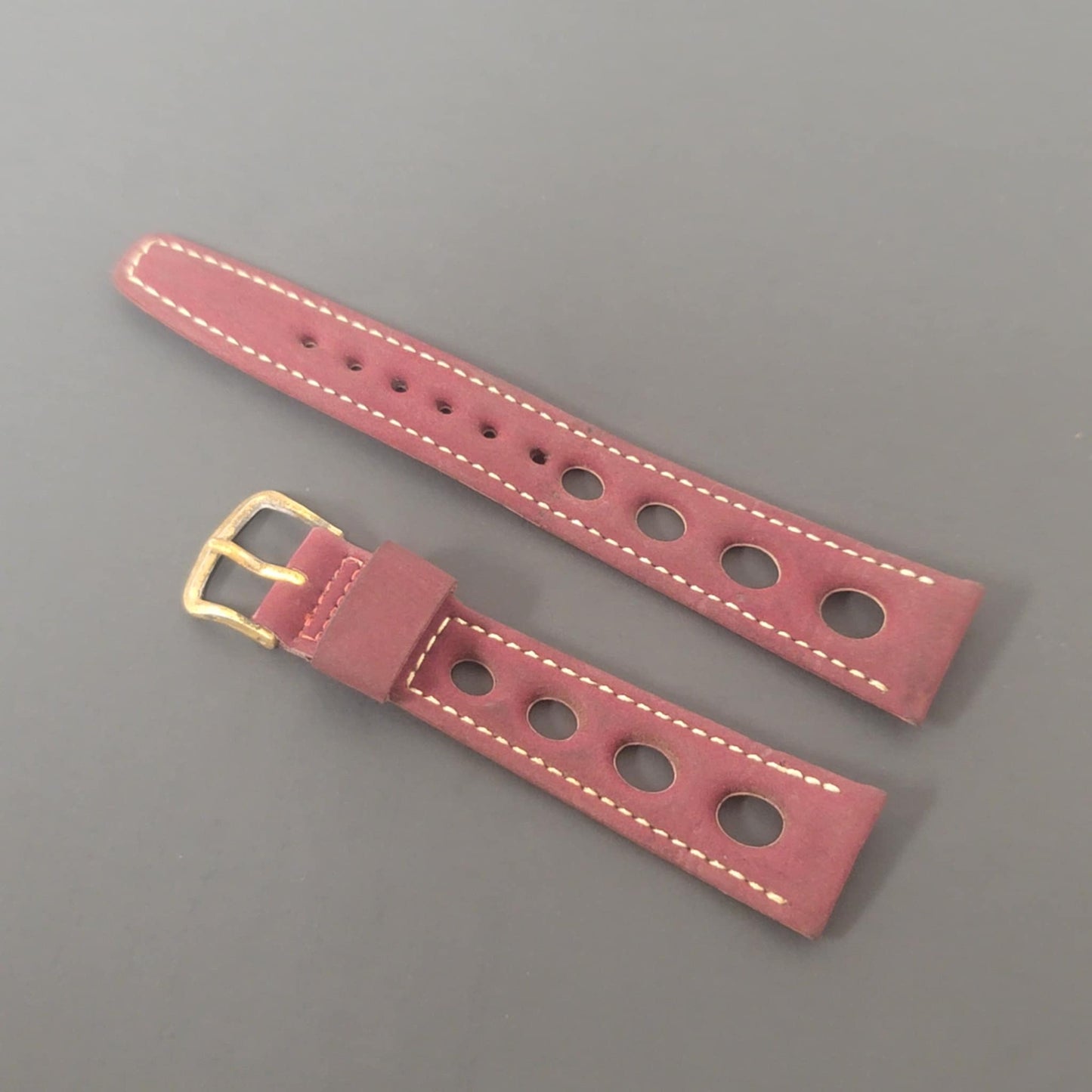 Pink leather watch strap with gold buckle on a gray background