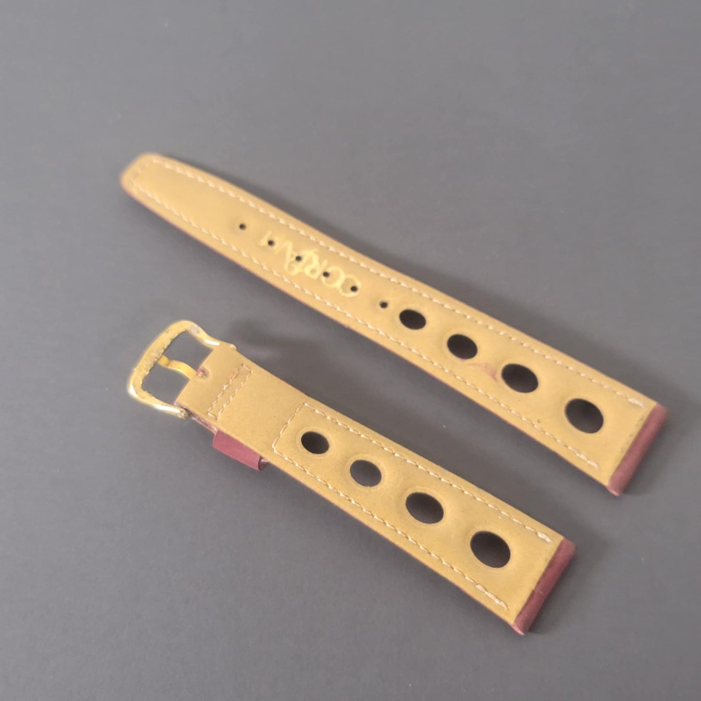 Gold watch strap with holes on a gray background