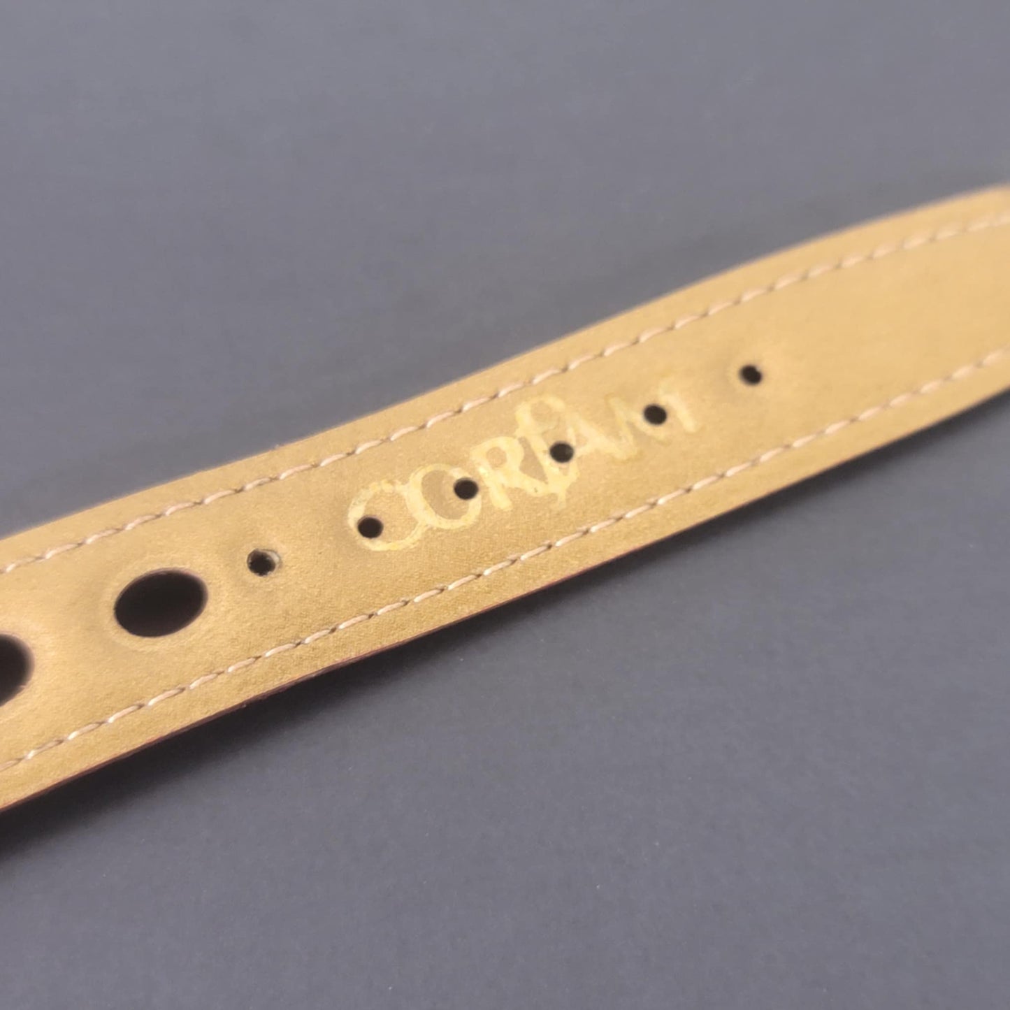 Beige leather strap with branding on a gray background