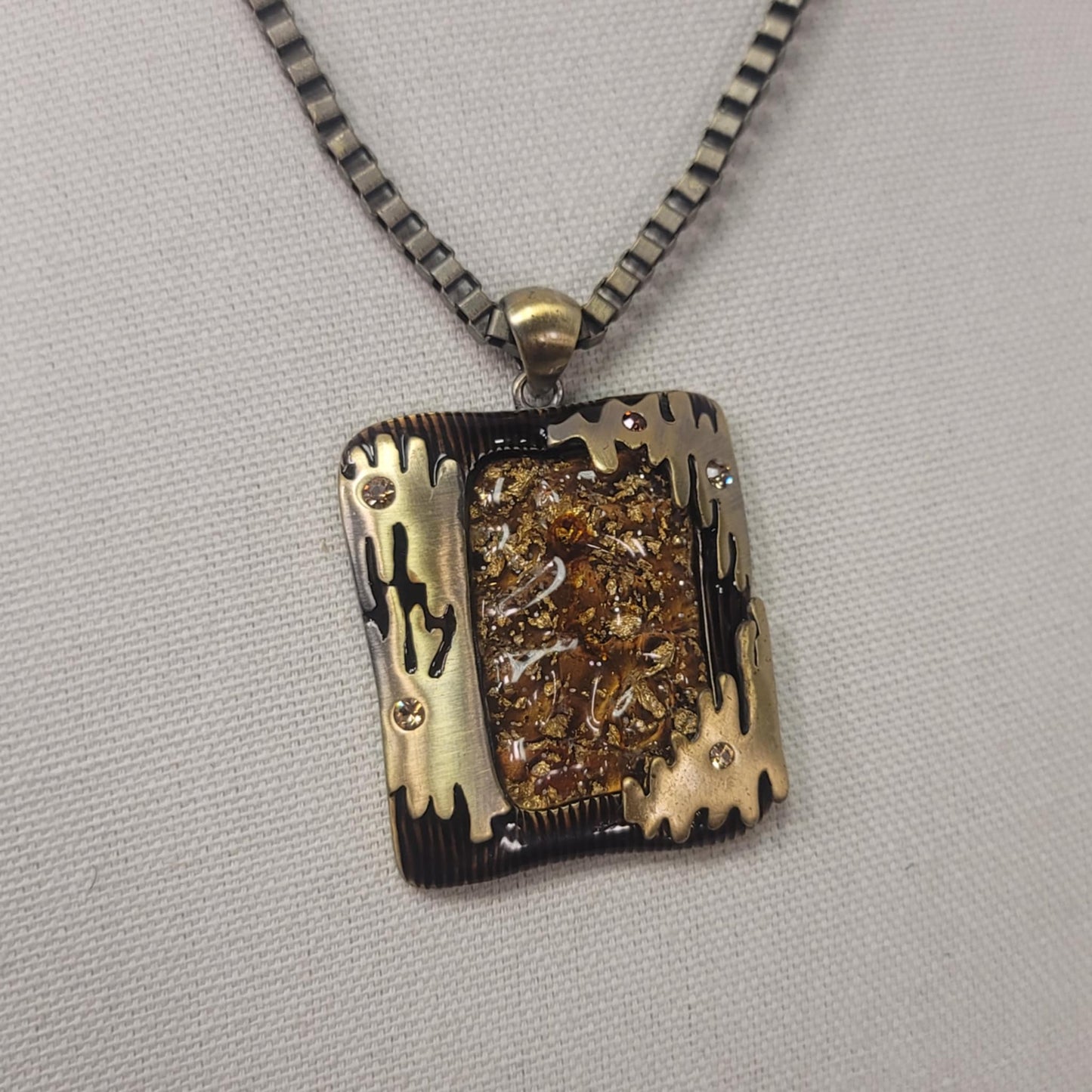 Necklace with a rectangular pendant featuring gold and black designs on a gray background