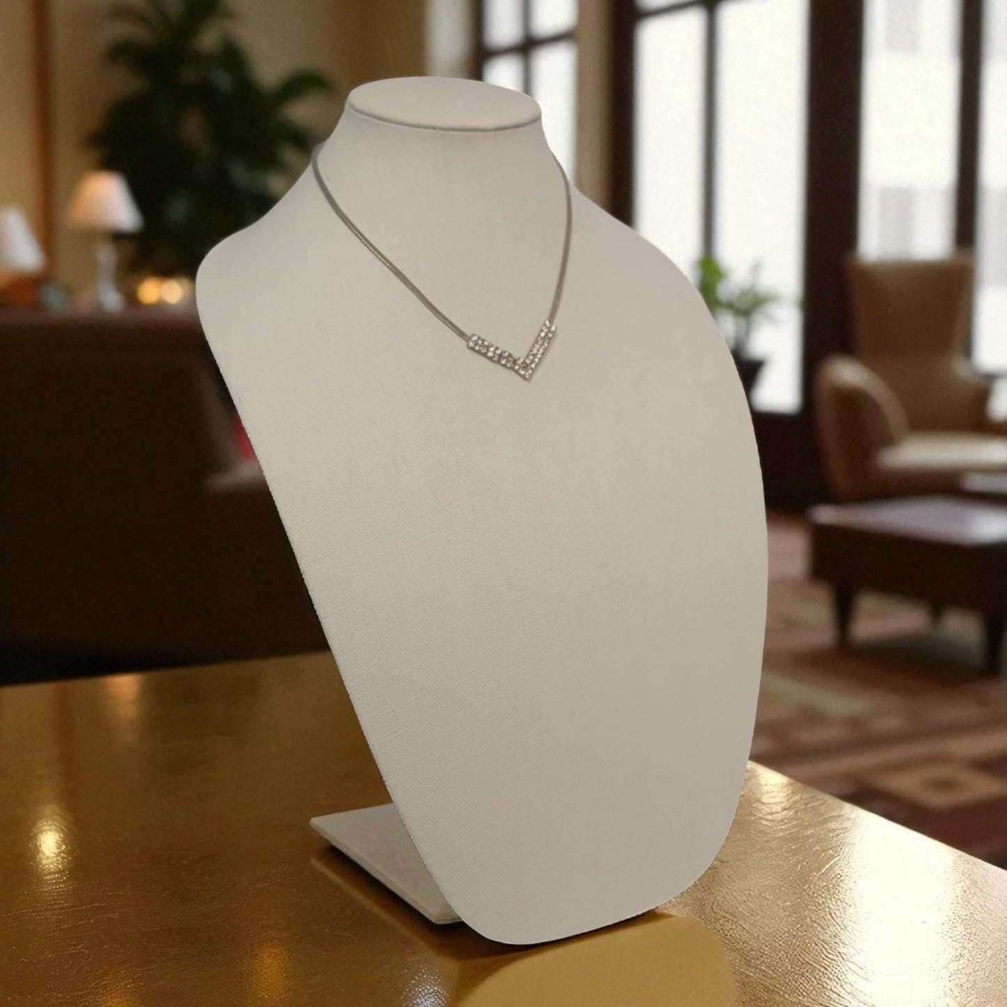 White jewelry display stand with a necklace on a wooden table in a room setting.