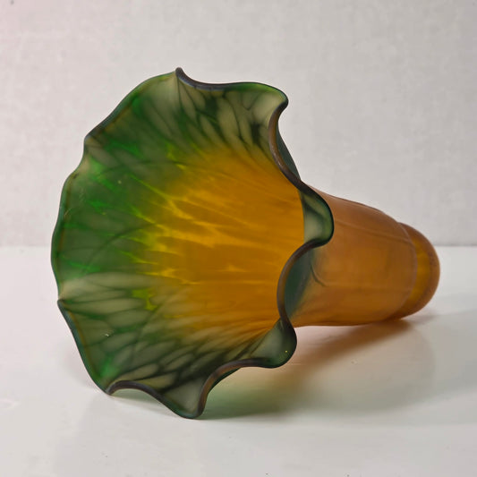Green and amber tulip-shaped glass lampshade with ruffled edge and mottled interior glow.