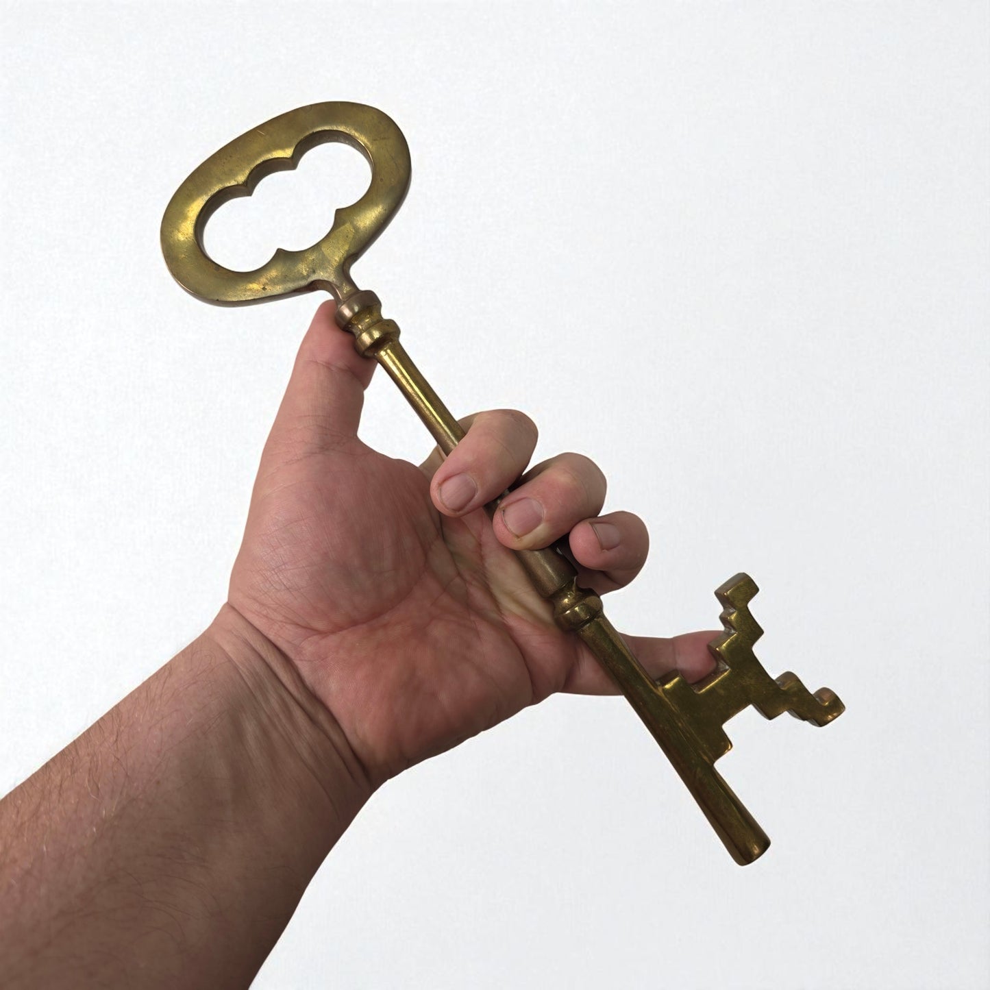 Hand holding a large brass key against a white background