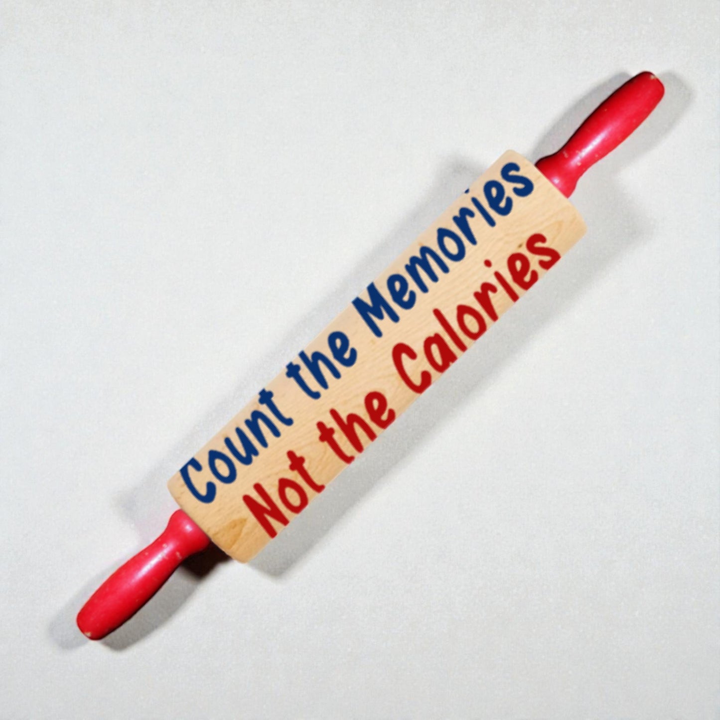 Red rolling pin with a wooden sign reading 'Count the Memories Not the Calories' on a white background