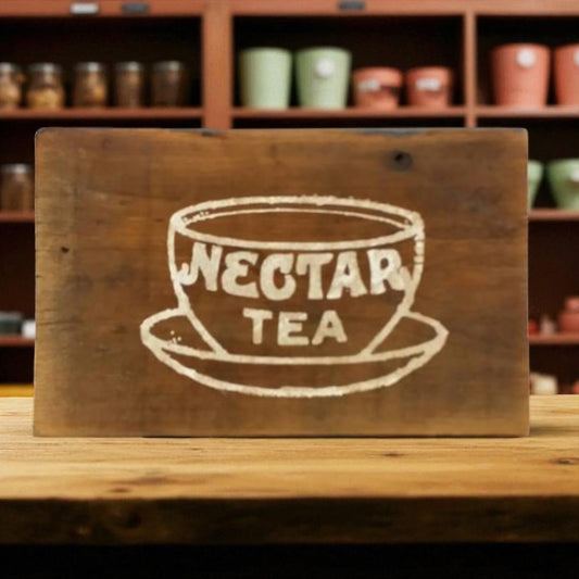 Wooden sign with 'Nectar Tea' design on a wooden surface with shelves in the background.