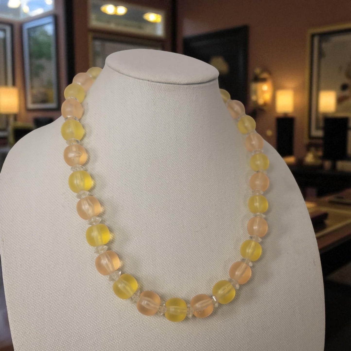 Necklace with yellow and pink beads on a mannequin bust in a room setting.