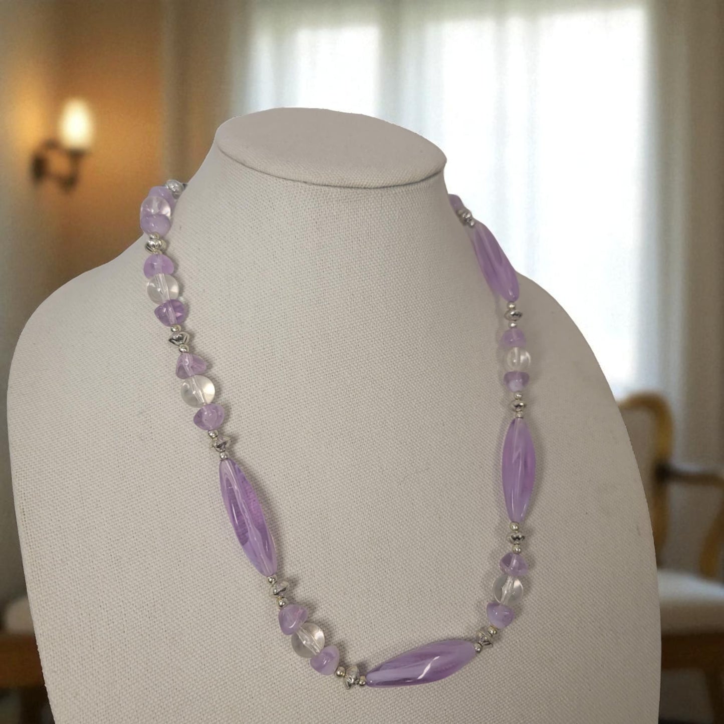 Necklace with purple and clear beads on a mannequin bust against a blurred indoor background