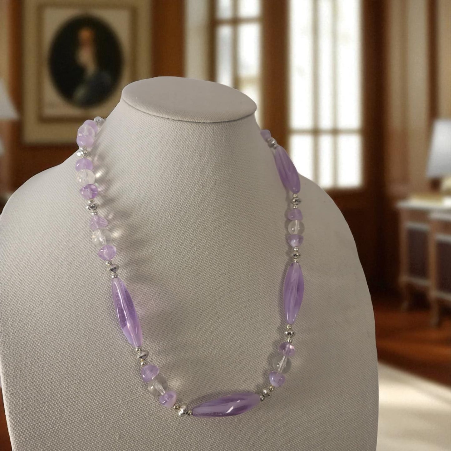 Necklace with purple and clear beads on a mannequin bust in a room setting.