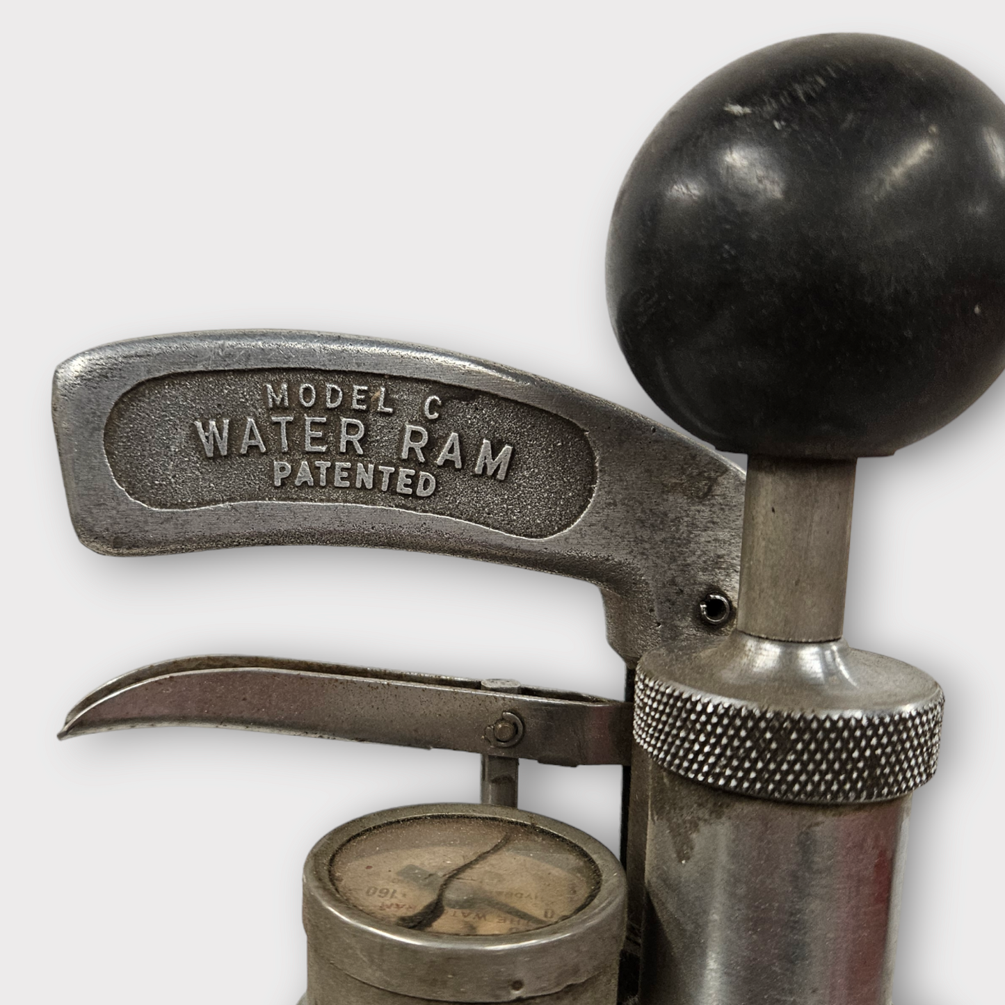 A silver-colored manual water ram plumbing tool with a black grip on the handle.