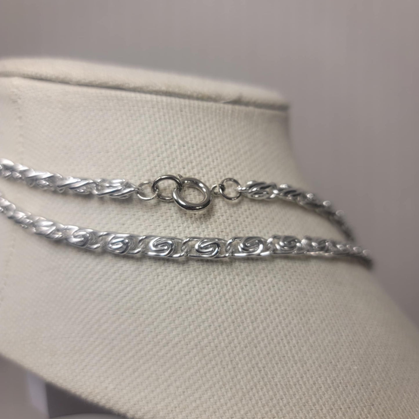 Silver chain necklace on a mannequin bust against a plain background
