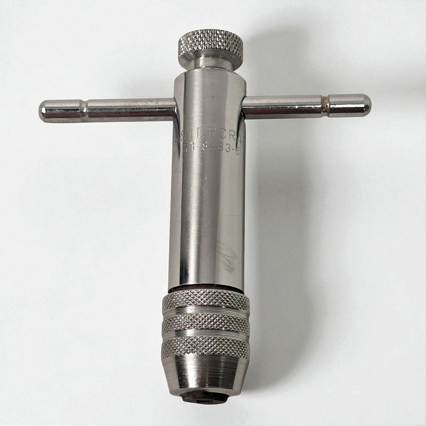 Metal t-handle drill bit on a white background