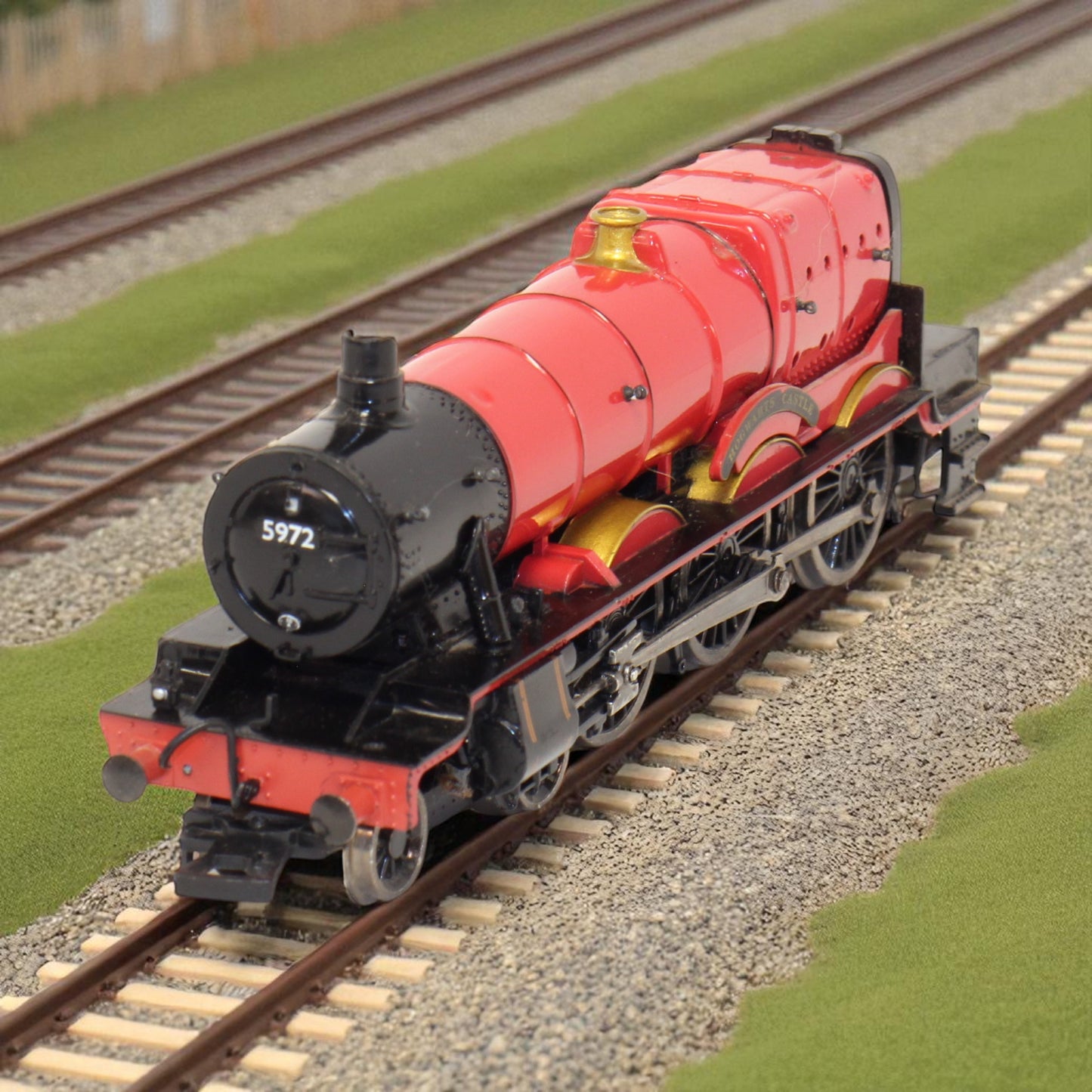 Model red steam locomotive on tracks with green grass and brown gravel.