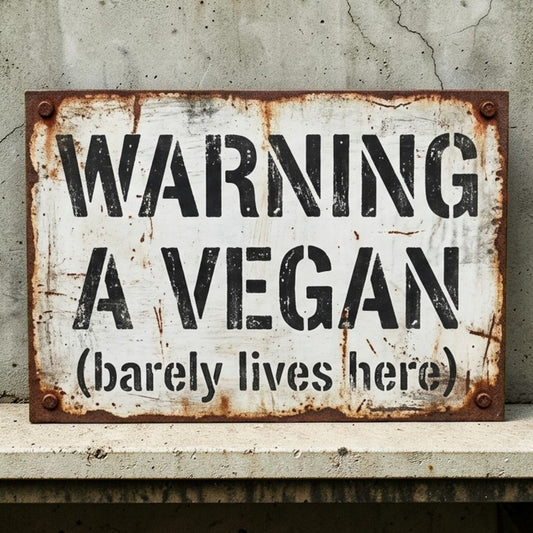 Rustic metal sign with text 'WARNING A VEGAN (barely lives here)' on a textured wall.