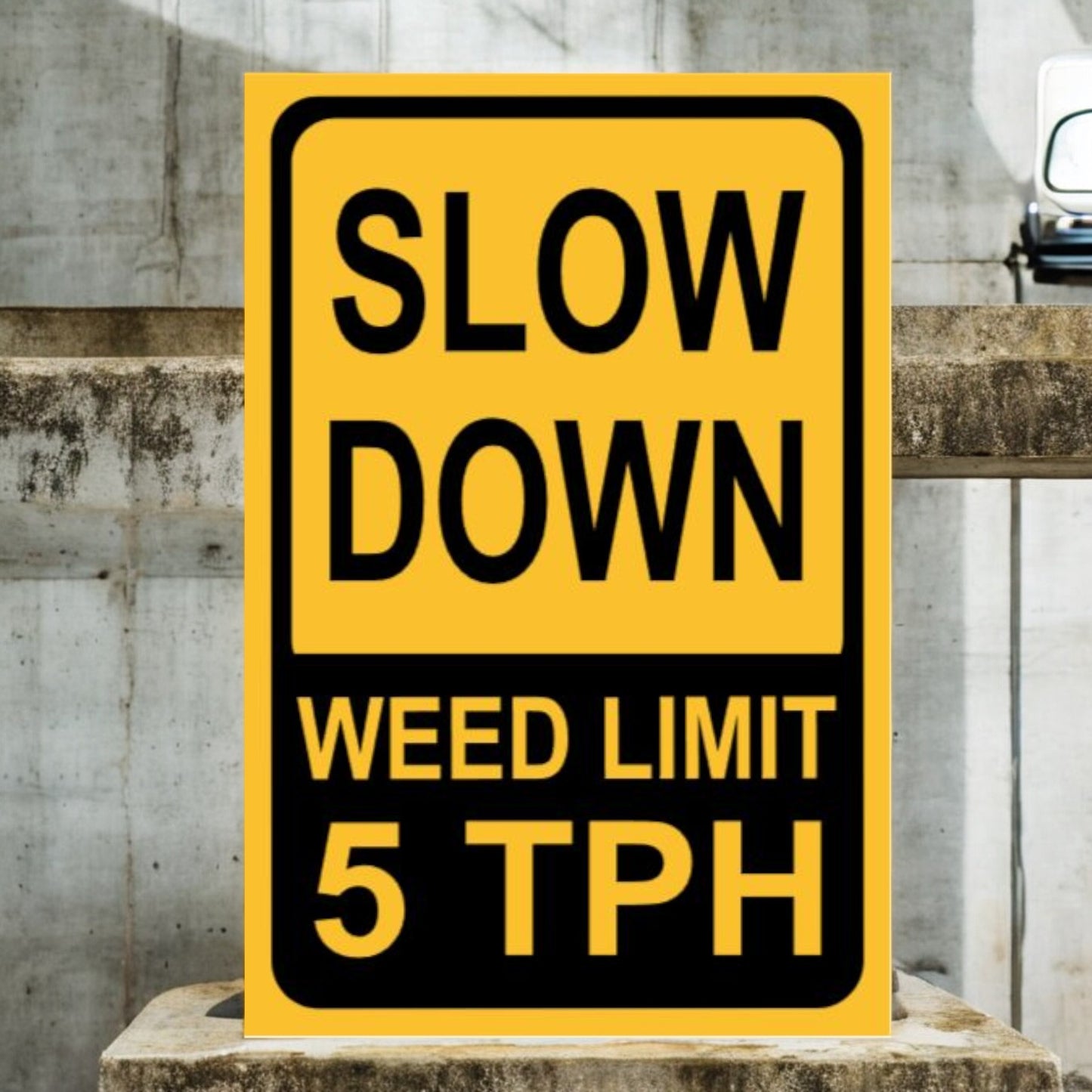 Yellow and black sign with 'Slow Down Weed Limit 5 TPH' text on a concrete surface.