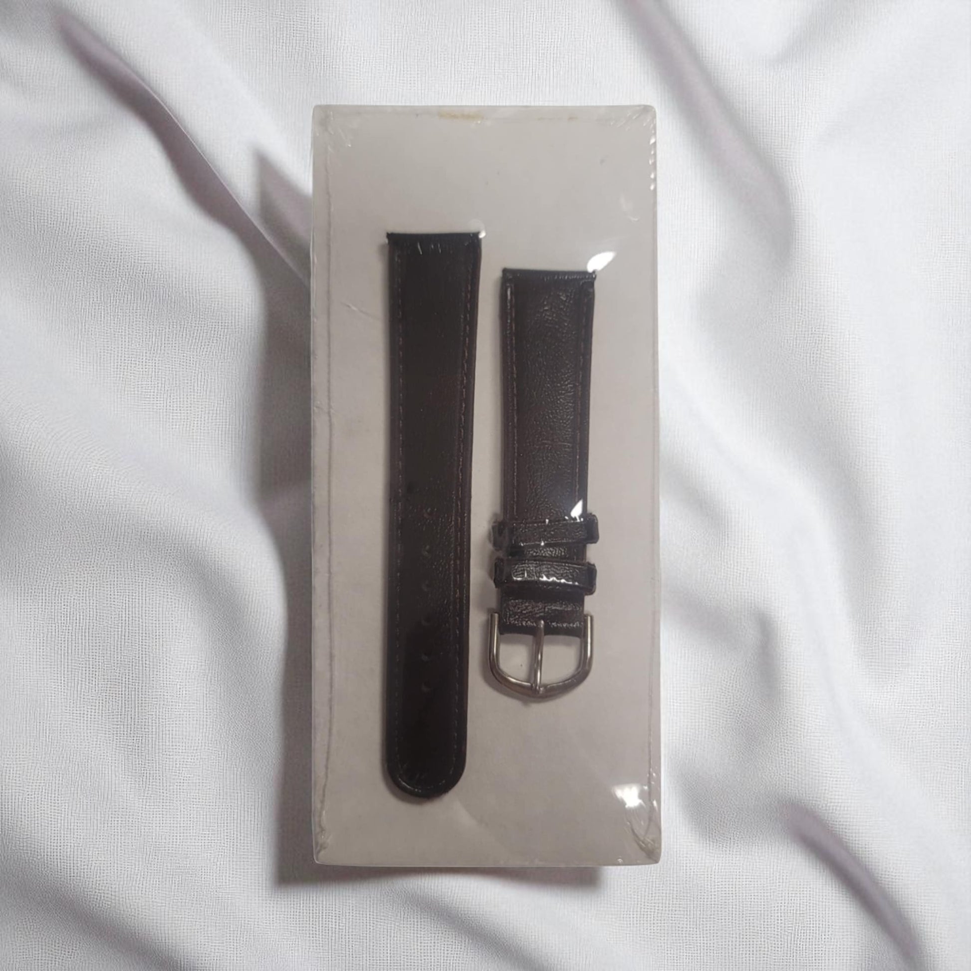 Black watch strap on a white card with a white background