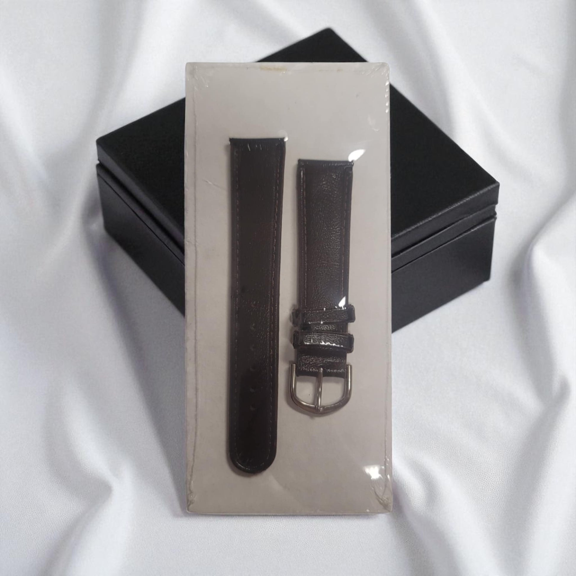 Black watch strap with silver buckle on a clear stand against a white background