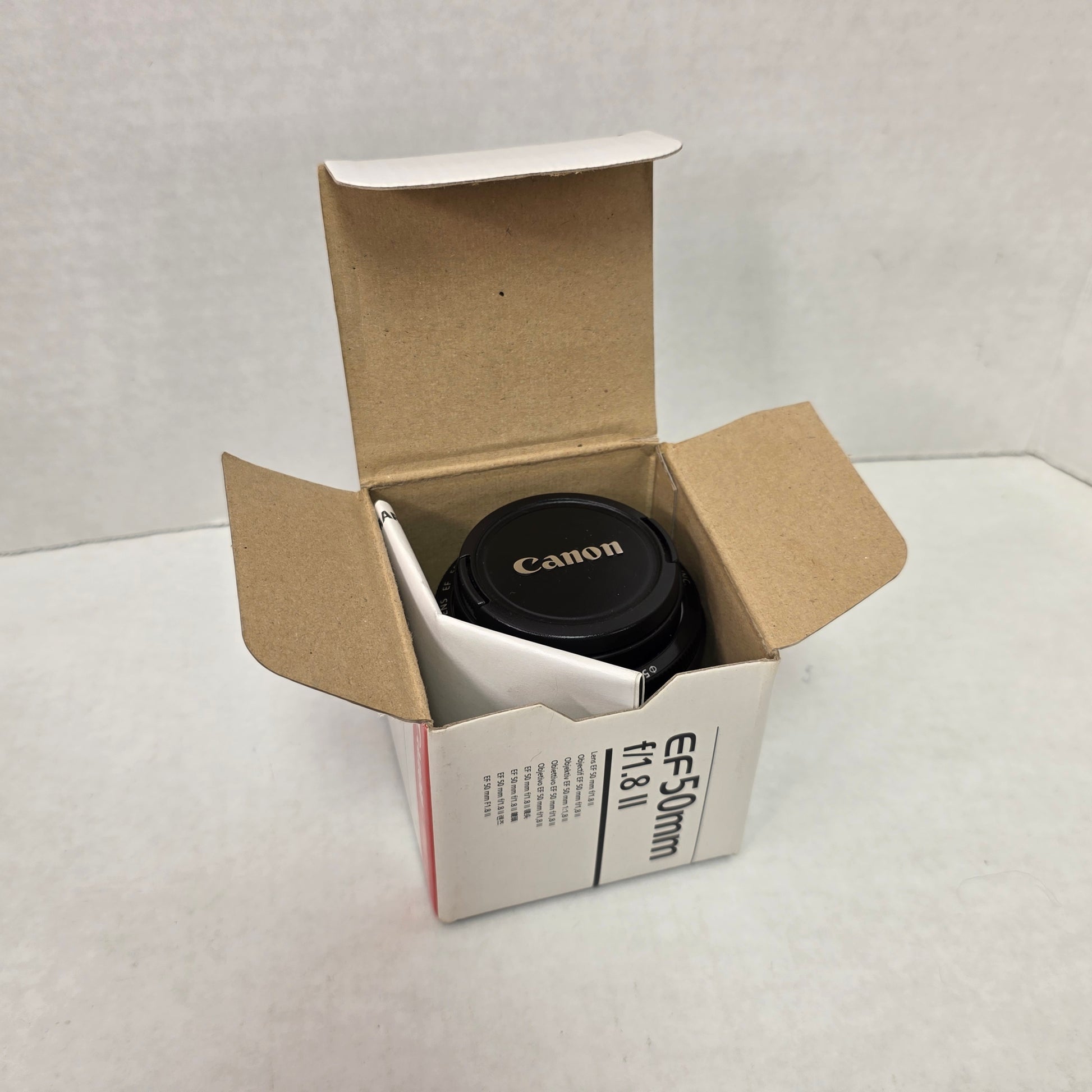 Canon camera lens in a cardboard box with a Canon product card on a light gray background