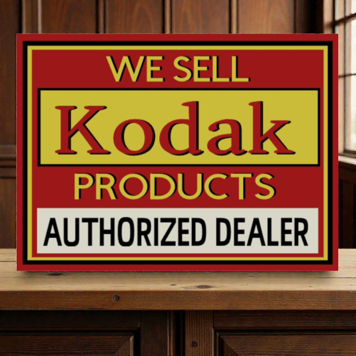 Vintage-style sign advertising Kodak products with a red border on a wooden surface.