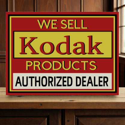 Vintage-style sign advertising Kodak products with a red border on a wooden surface.