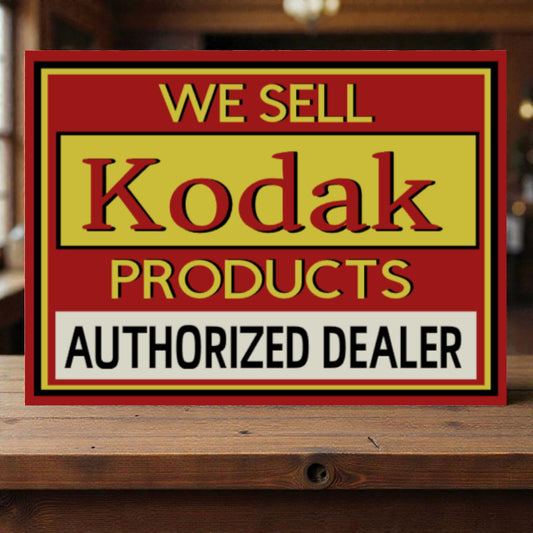 Vintage-style sign advertising Kodak products with a red border on a wooden surface.