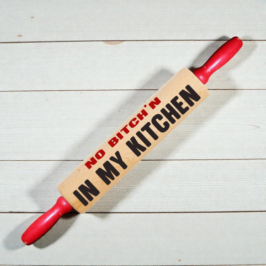 Rolling pin with 'No Bitch'n in My Kitchen' text on a wooden surface