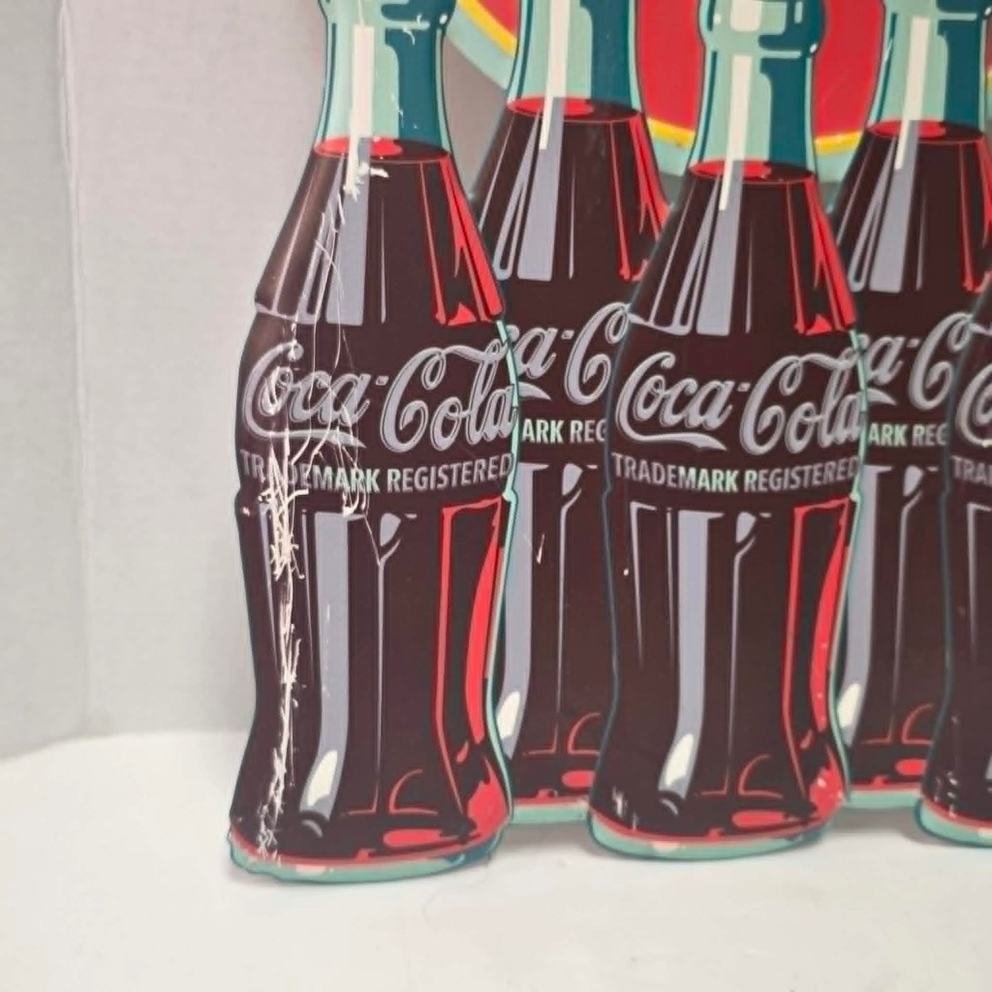 Large vintage Coca-Cola embossed metal sign with five bottles and advertising design.
