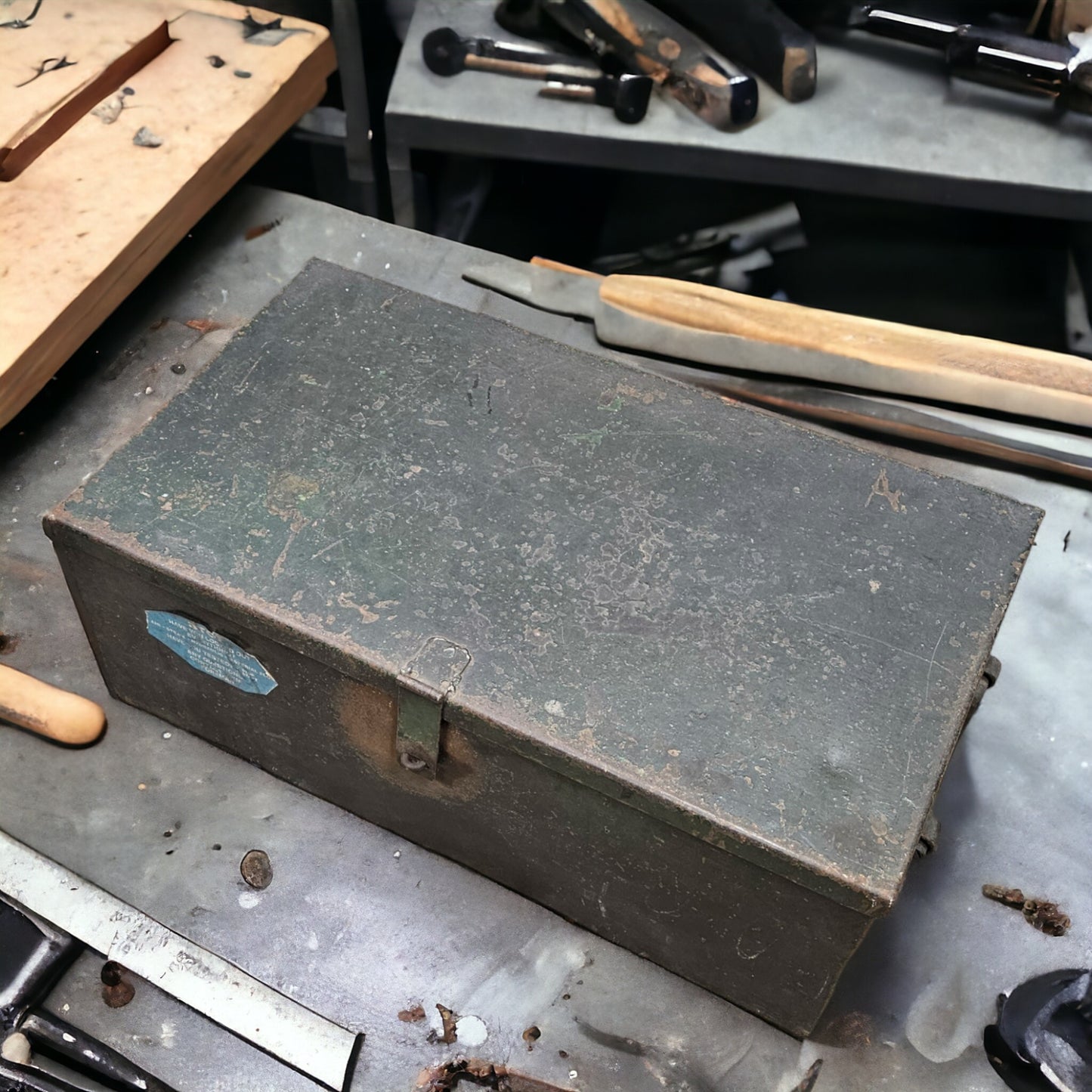 A large metal tool storage container with a latch, placed on a workbench among other tools.