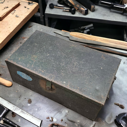 A large metal tool storage container with a latch, placed on a workbench among other tools.