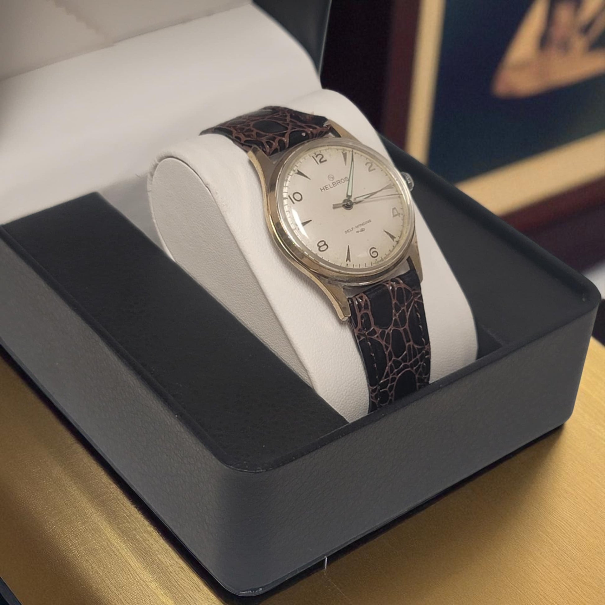 Vintage watch with a dark strap on a white cushion in a black box