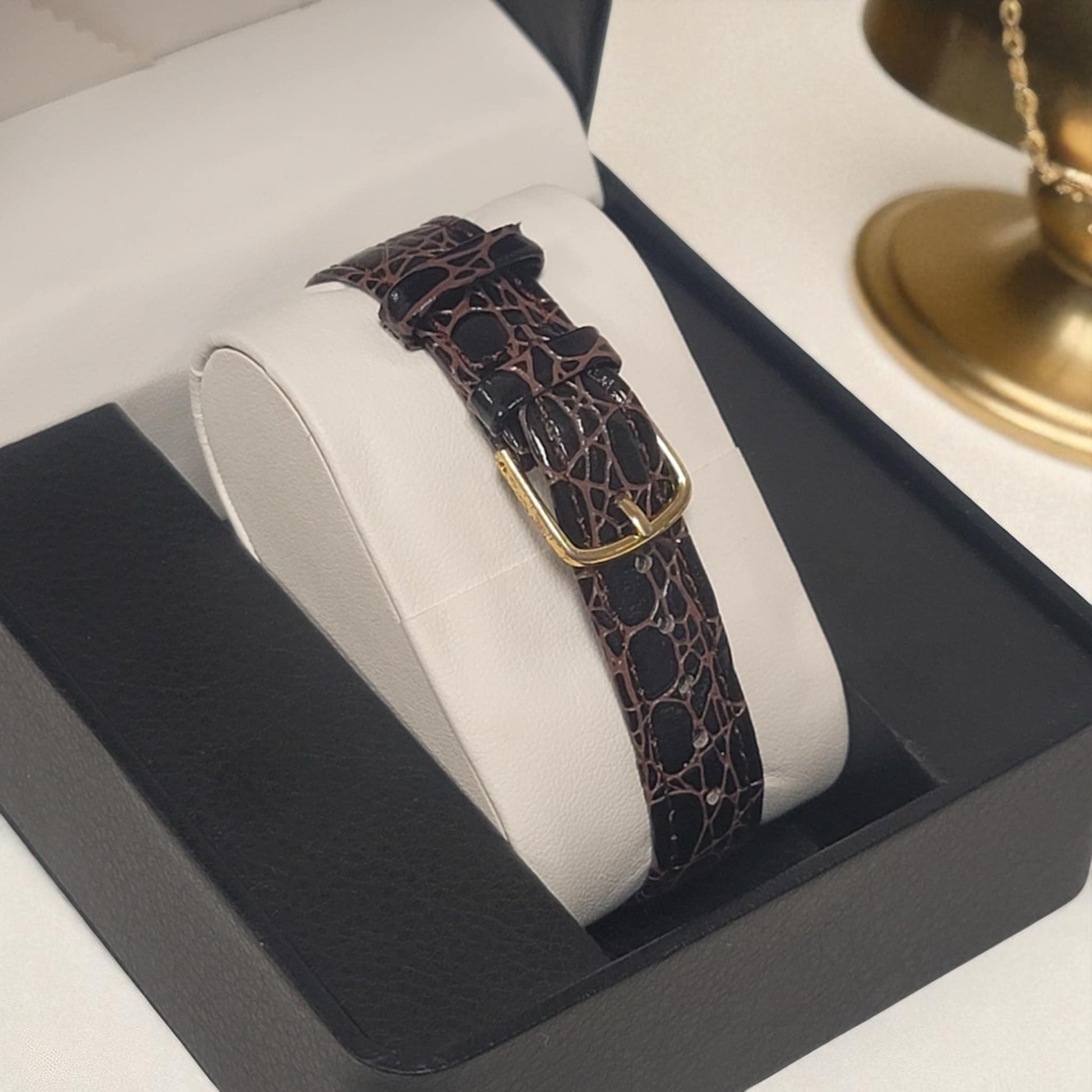 Watch strap with gold buckle on a white cushion in a black box