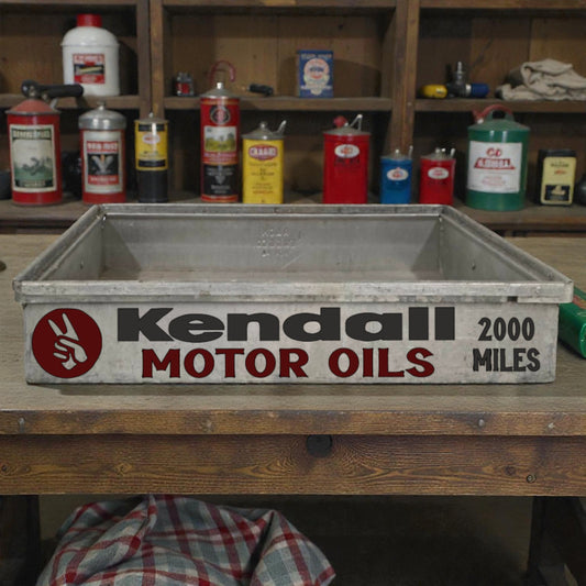 Vintage Kendall Motor Oils oil pan on a wooden shelf with various cans in the background.