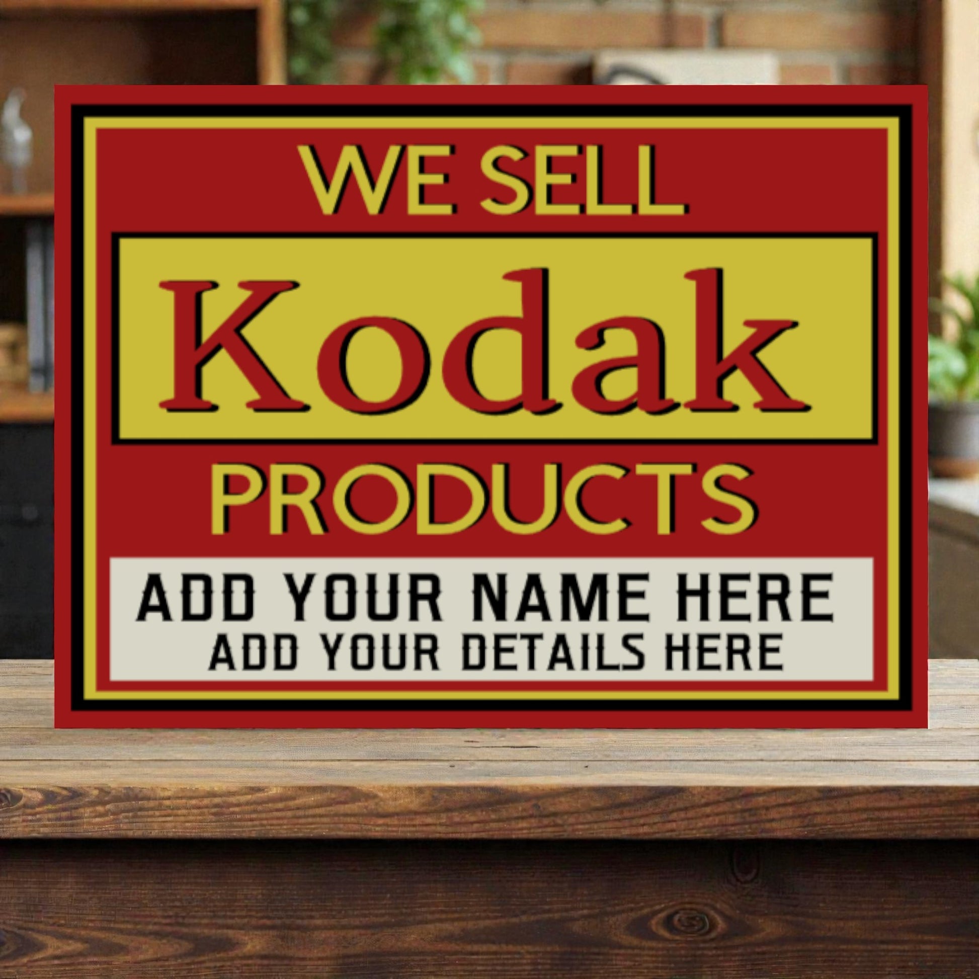 Vintage-style sign advertising Kodak products with a red border on a wooden surface.
