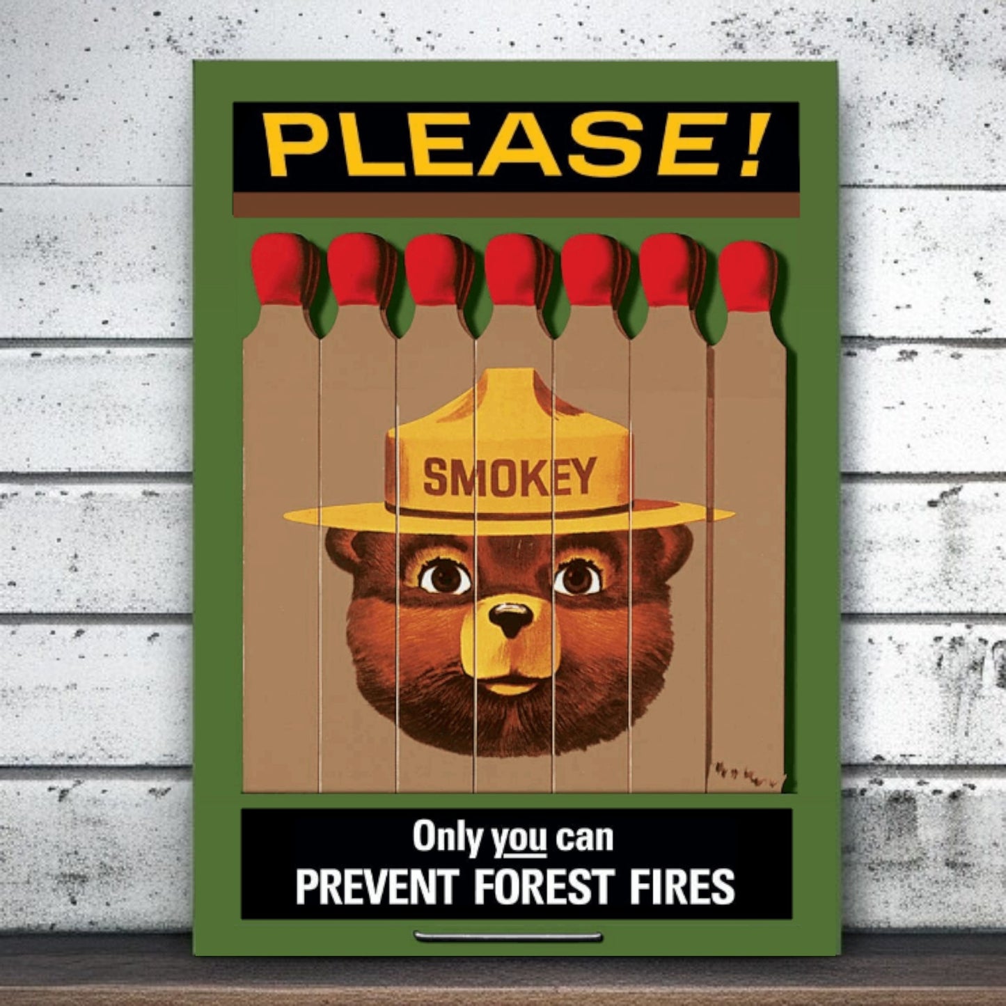 Smokey Bear poster with matches and 'Please!' text on a wooden surface.