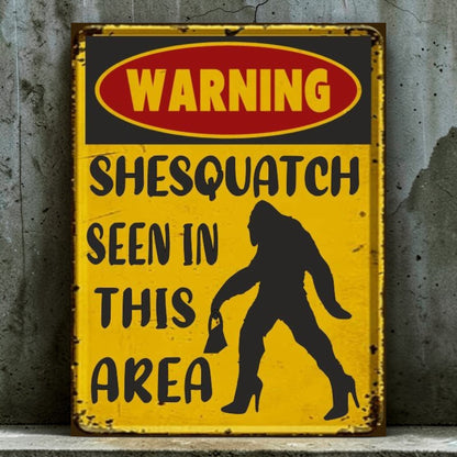 Vintage-style metal sign with a warning about 'Shesquatch' seen in the area on a textured wall background.
