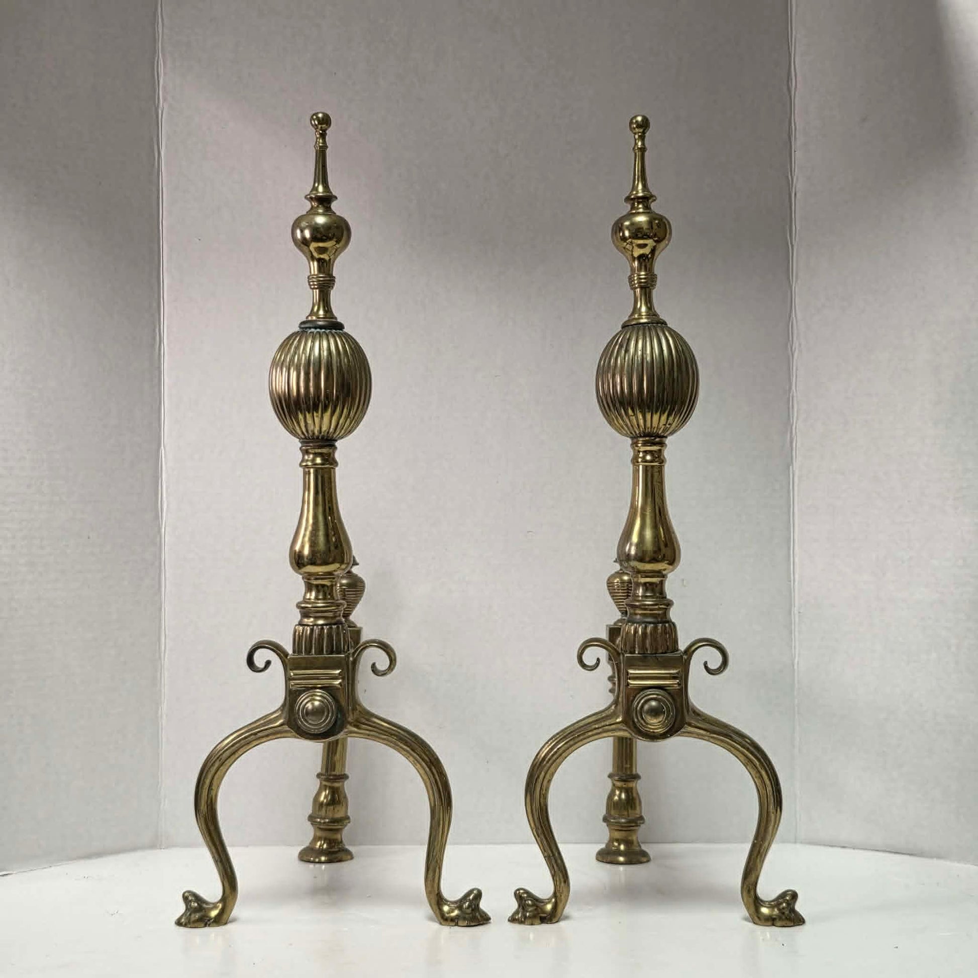 Victorian brass and bronze fireplace andirons with ornate figural bases and fluted ball finials.