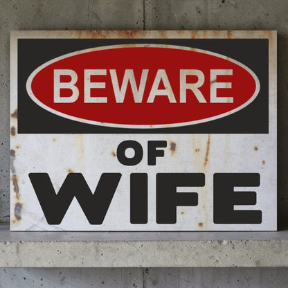 Rust-covered sign with 'Beware of Wife' text on a concrete wall.