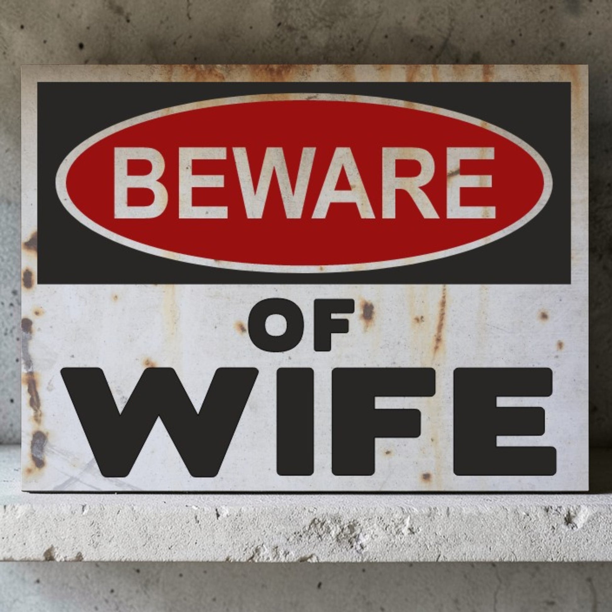 Rust-covered sign with 'Beware of Wife' text on a concrete wall.